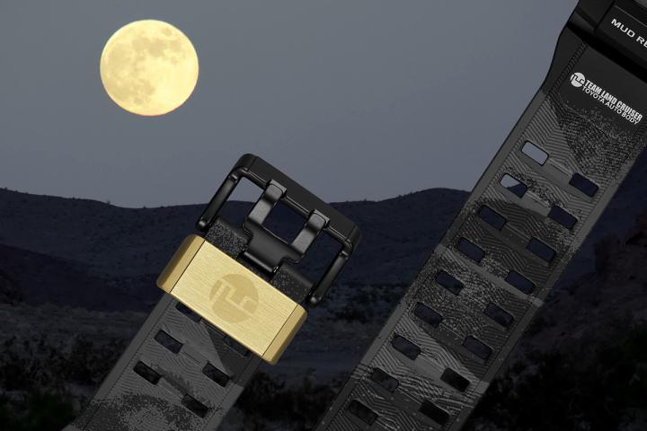 黑色生物质树脂表带印有满版沙丘纹理营造夜间沙漠意象，搭配象征满月的金色且饰有 TCL 车队 logo 的表带扣环，呼应车队在夜间赛段竞速与月光下进行机械维修的赛事氛围。