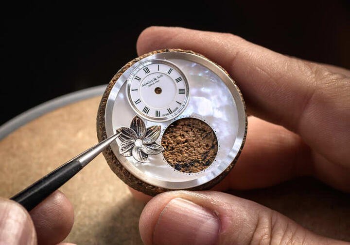 制表师在珍珠母贝面盘上，将银制莲花一朵一朵刻划而成并镶嵌固定于面盘上