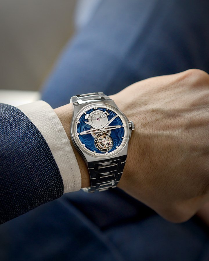 Antarctique Tourbillon Titanium Cosmic Blue 在深邃蓝色背景映衬下，修长的传动桥与镂空发条桥的手工倒角抛光边缘，以及陀飞轮框架上方支臂的缎面处理，共同营造出丰富而细腻的光影变化。