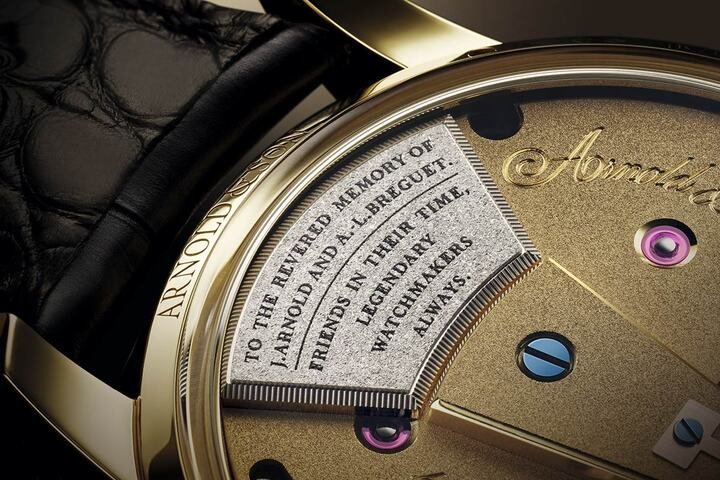 Constant Force Tourbillon 11恒定动力陀飞轮腕表倒角饰面发条盒桥板上，刻有手工雕刻的铭文：“To the revered memory of John Arnold and Abraham-Louis Breguet. Friends in their time, legendary watchmakers always.”(纪念约翰·亚诺与亚伯拉罕–路易·宝玑，一世的挚友，永远的传奇制表大师)，赞颂了两位制表巨匠的深厚友谊与卓越贡献。
