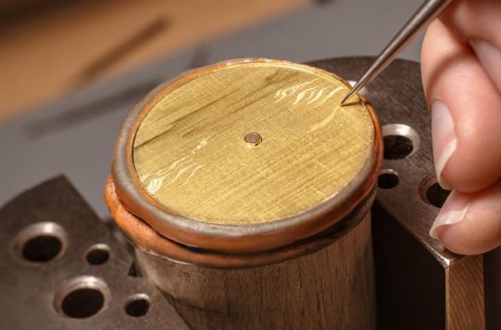 18K 黄金面盘先以手工雕刻建立景深层次，雾面与亮面交错，铺陈英雄征战场景的动感背景。