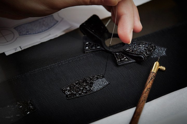 Nœud de Camélia 刺绣手环表蝴蝶结由 Lesage 工坊绣制而成，每一件作品都由一位工匠负责精心制作，在黑色雾面罗缎绣上约数百颗内镀精金的玻璃圆珠，整个过程需耗时约 8 小时，刺绣也同时赋予蝴蝶结立体感、质感、和视觉深度，展现高级手工艺的精湛所在。