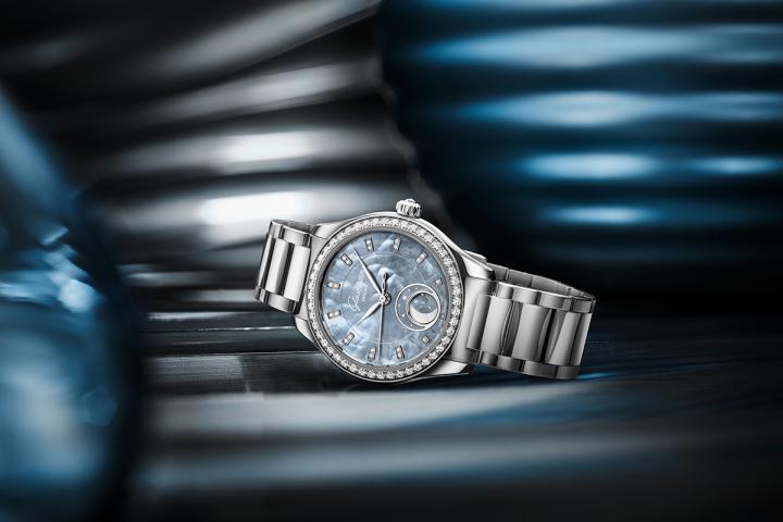 表壳外圈镶嵌 48 颗明亮型切割钻石，搭配珍珠母贝表盘上手工镶嵌的明亮型切割钻石时标，与 6 点钟方向月相显示周围的小巧银色星辰相互辉映。