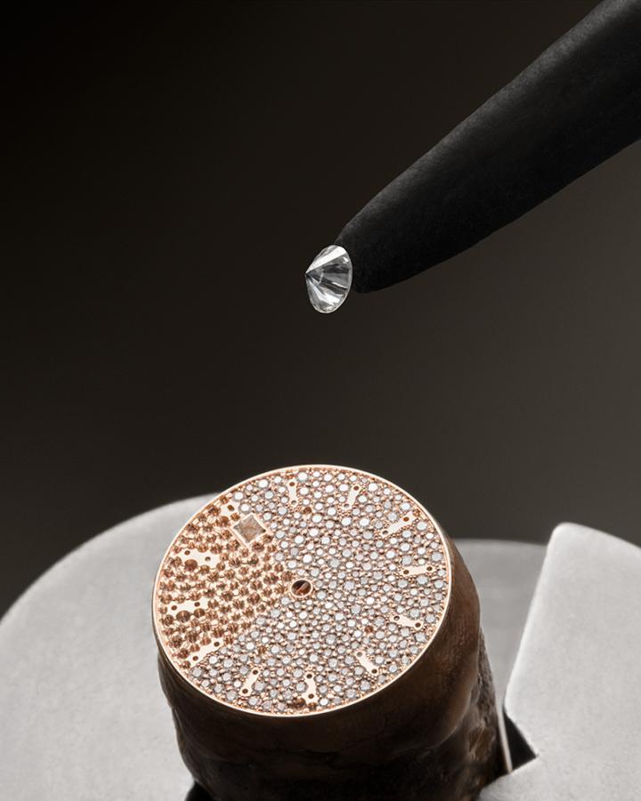 表盘采用优雅而实用的简约设计，仅保留基本时间与日期显示，令 314 颗雪花镶嵌明亮式切割钻石 (总重约 1.65 克拉) 得以尽绽璀璨光华。珠宝镶嵌大师需将不同尺寸的钻石，交错满铺于表盘的金质基底上，看似随意散落，实则饱含匠心。