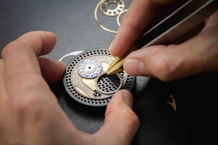 表盘盖上激光切割的 3N 黄金支撑环，形成装饰边框，仿效了凡尔赛宫镜厅内的抛光黄铜细节。陀飞轮的框架则重现了凡尔赛宫小堂内随处可见的彩绘玻璃图案，包括百合花饰图案。