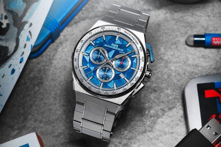 两枚按把的设计带有强烈识别度：2 点钟方向的 Start/Stop 按键刻上防滑纹理，为指尖带来清晰回馈感；4 点钟位置的 Reset 按键则以极简造型收尾，平衡视觉张力。铝合金外圈镌刻 Tachymeter 测速刻度，是速度爱好者之间的默契暗号，也是一股藏在腕间的力量。