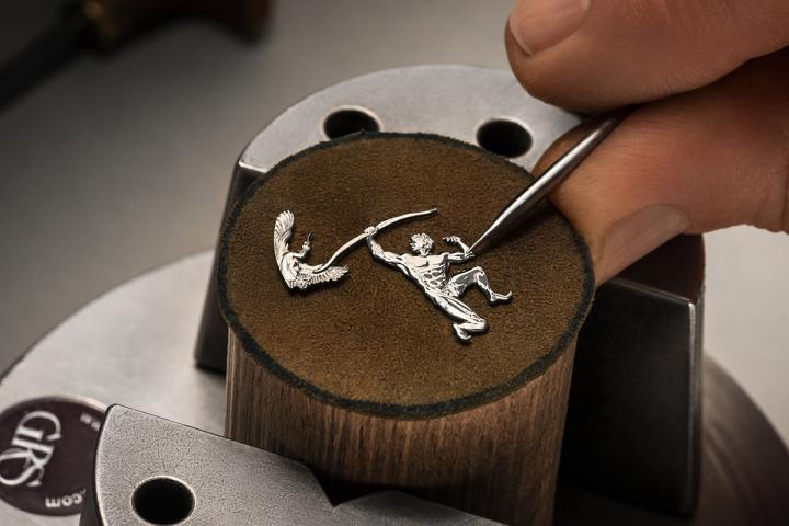 Heracles 与凶猛神兽殊死搏斗的惊险一幕，以 18K 白金手工微雕呈现，迸发出呼之欲出的磅礴力量与气势。在厚度仅 0.5 毫米的图案中，手工雕刻大师纤毫毕现地刻划出丰富细节，从 Heracles 的肌肉线条、面部神情和卷曲的发丝，到神兽的皮毛、鳞片或羽翼，营造出饱满的立体感与动态张力。每一件微雕作品耗时约 40 小时。