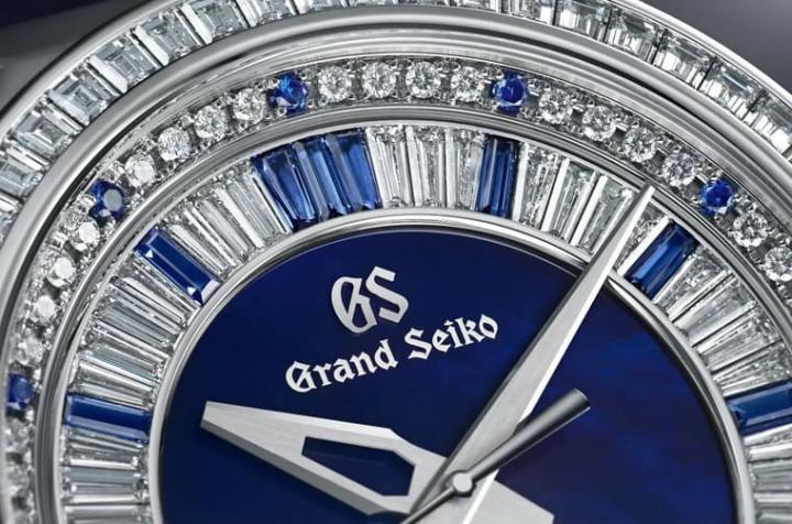 面盘内侧的珍珠母贝染上代表GRAND SEIKO的深蓝色，同时外圈两处也改用矩形切割与圆形切割蓝宝石点缀，搭配镶嵌在同一处的钻石，透过对比突显蓝宝石作为时标与分钟刻度的作用。
