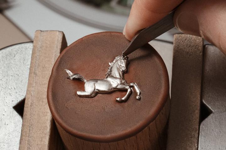 骏马和岩石图案由手工雕刻大师以 18K 白金或粉红金材质雕琢而成，入微刻画出马鬃和马尾等传神细节，并通过手工氧化着色工艺，进一步凸显图案的纹理质感和轮廓线条。